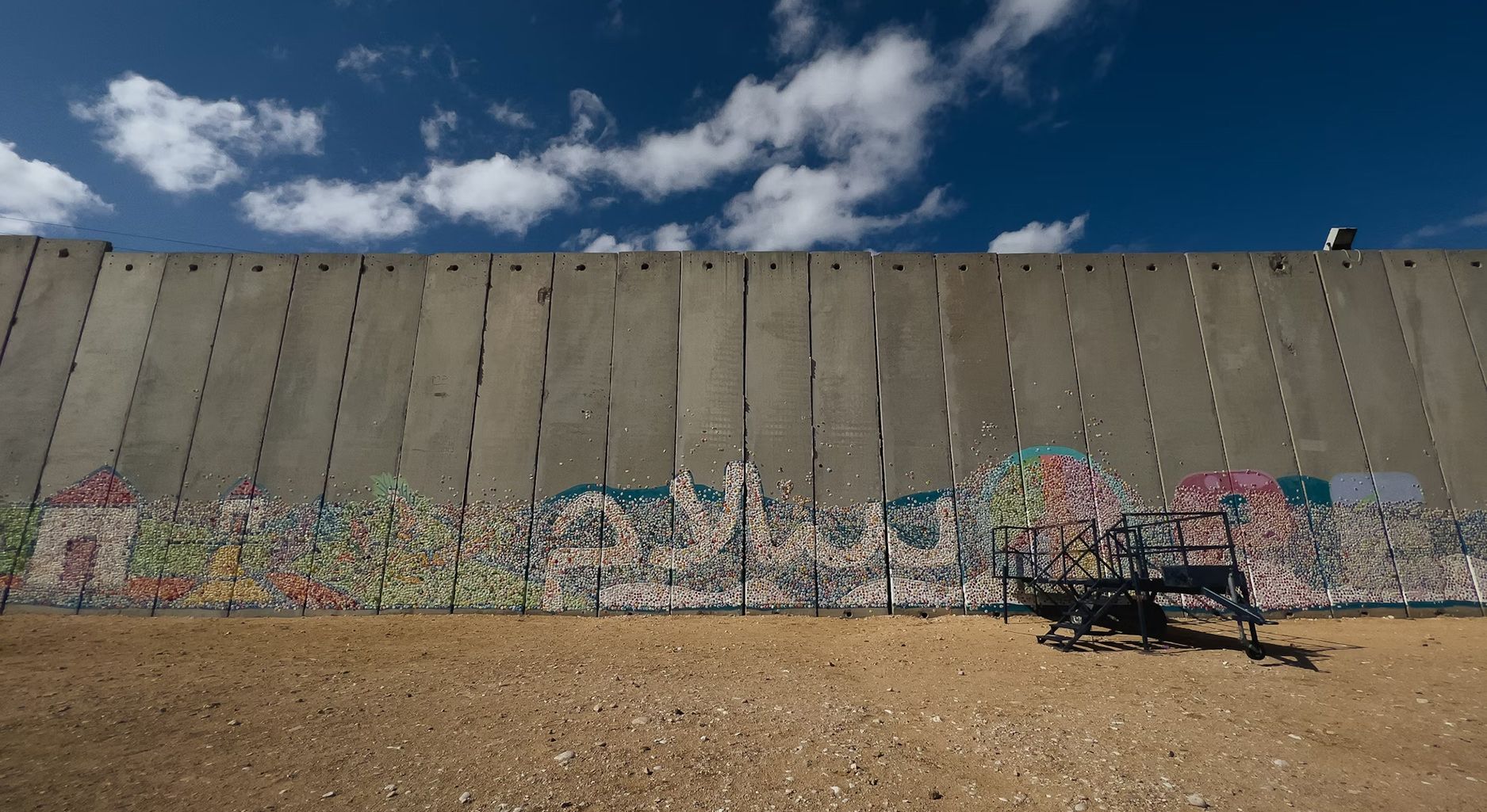 a concrete wall with graffiti stands on desert sand against blue sky