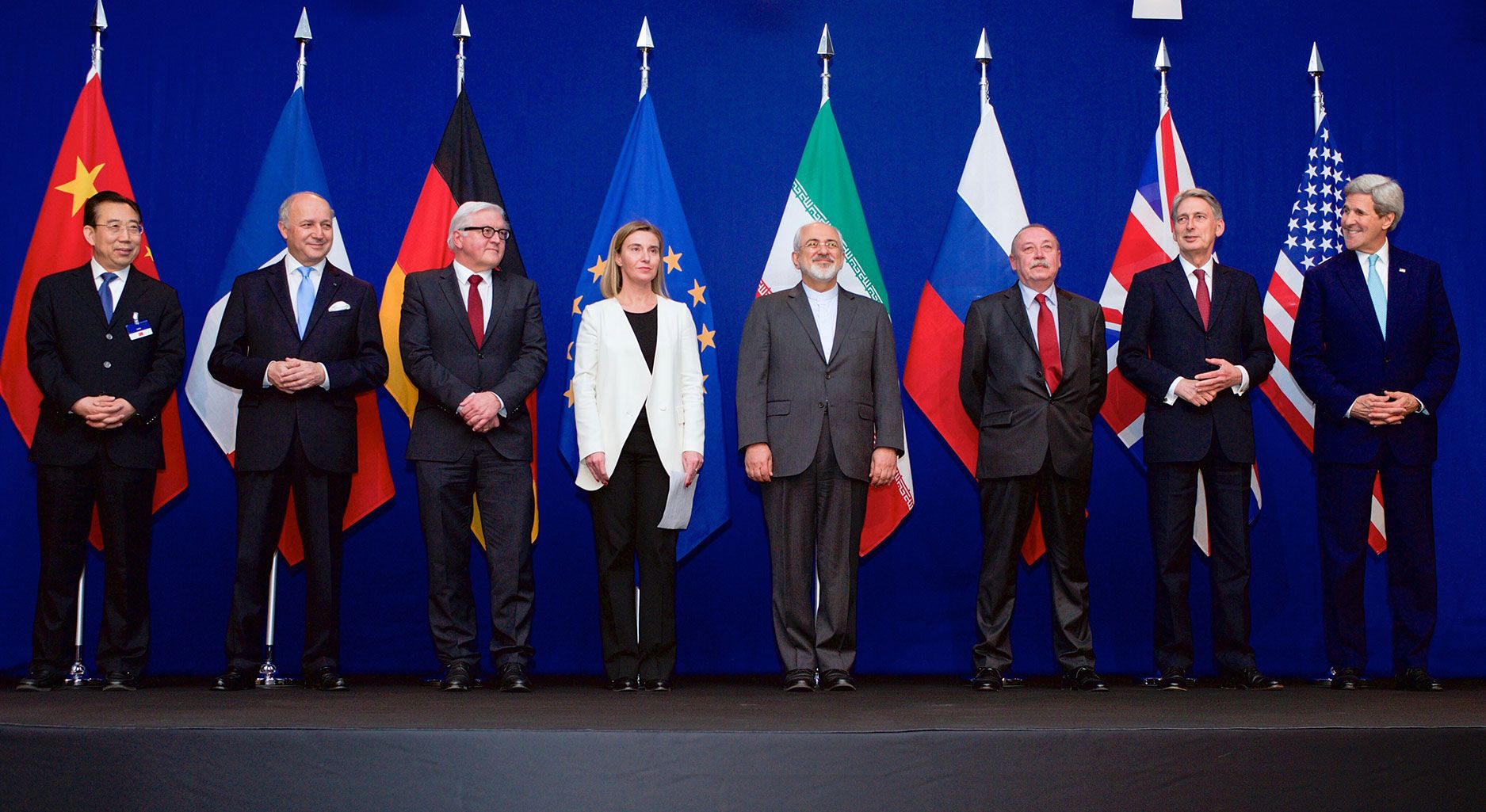 Eight men and women (who are the foreign ministers of the countries of the UN Security Council, the European Union and Iran) stand in front of their flags.