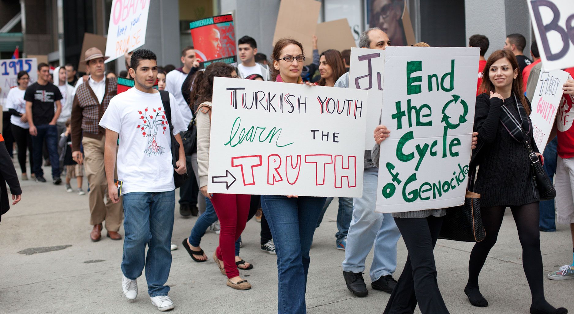 a group of people protest in front of the Turkish embassy holding signs saying: Turkisn Youth learn the Truth or End the Cycle of Genocide