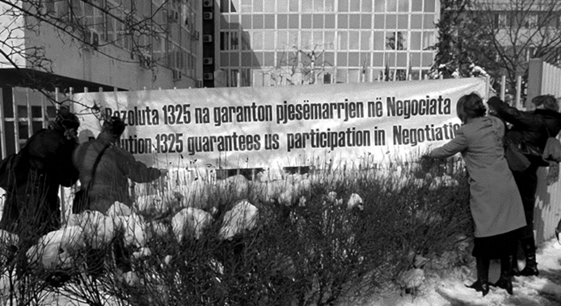 Frauen, die ein Banner aufhängen mit einer albanischen Aufschrift und der englischen Übersetzung „Resolution 1325 guarantees us participation in Negotiation.“
