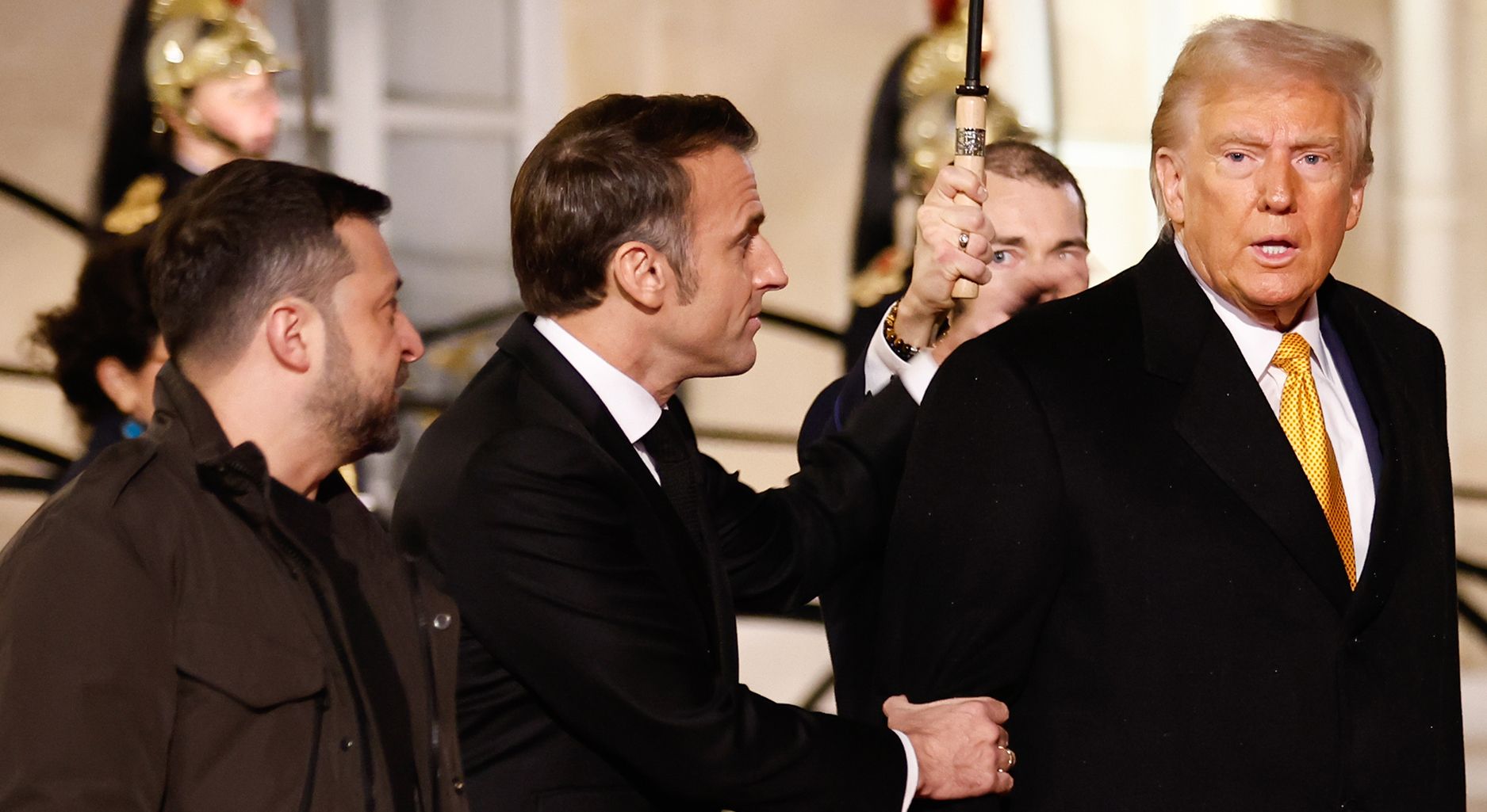 Zelensky and Macron look at Trump, who turns slightly, Macron grabs Trump's arm.