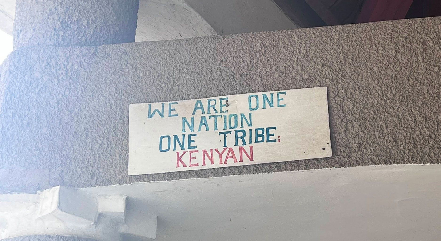 Plaque on a wall reading: We Are one Nation One Tribe Kenyan.