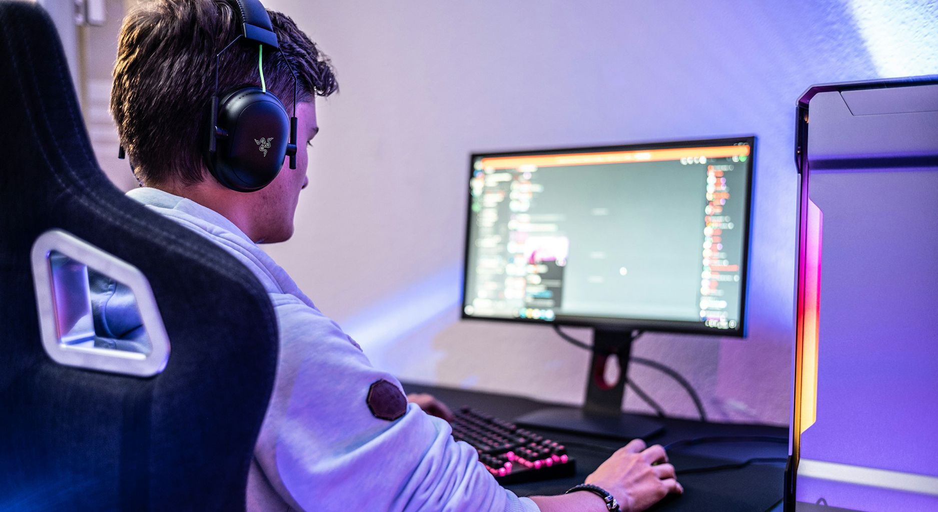 Ein Mann mit Kopfhörern sitzt vor einem Gamer-Bildschirm auf dem man diffus Chats erkennen kann