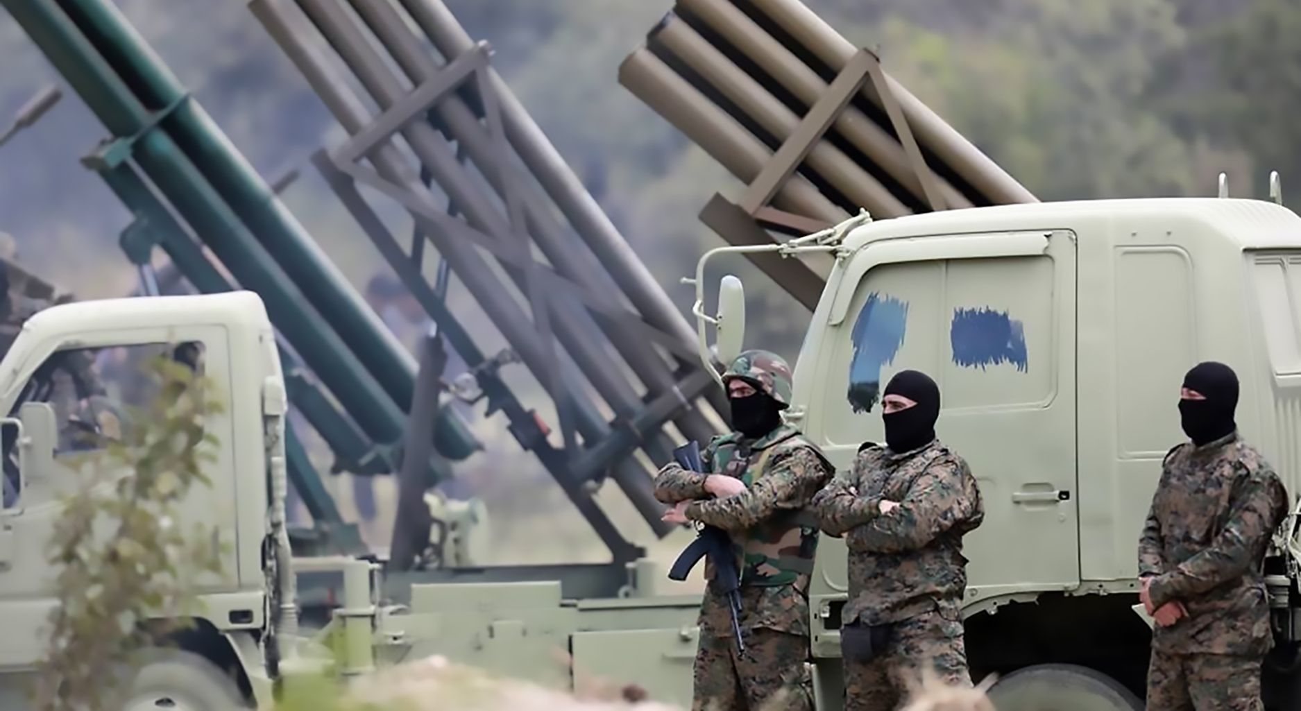 Three armed and masked men in military uniforms in front of a vehicle.