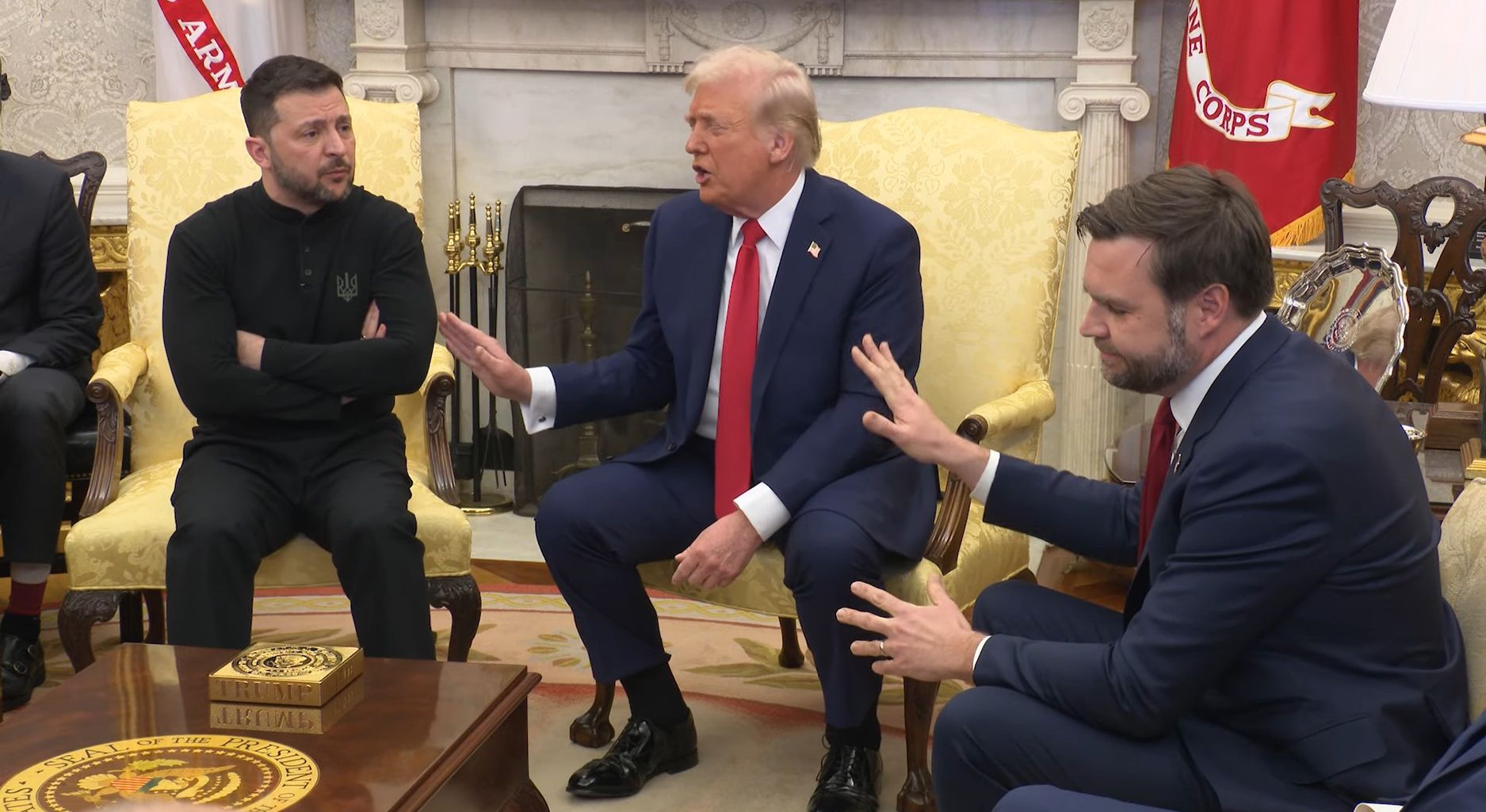 Wolodymyr Selenskyj, Donald Trump und JD Vance im Oval Office. Selenskyj hat die Arme verschränkt, Trump und Vance strecken ihm abwehrende Handflächen entgegen, Vance hat das Gesicht leicht abgeneigt.