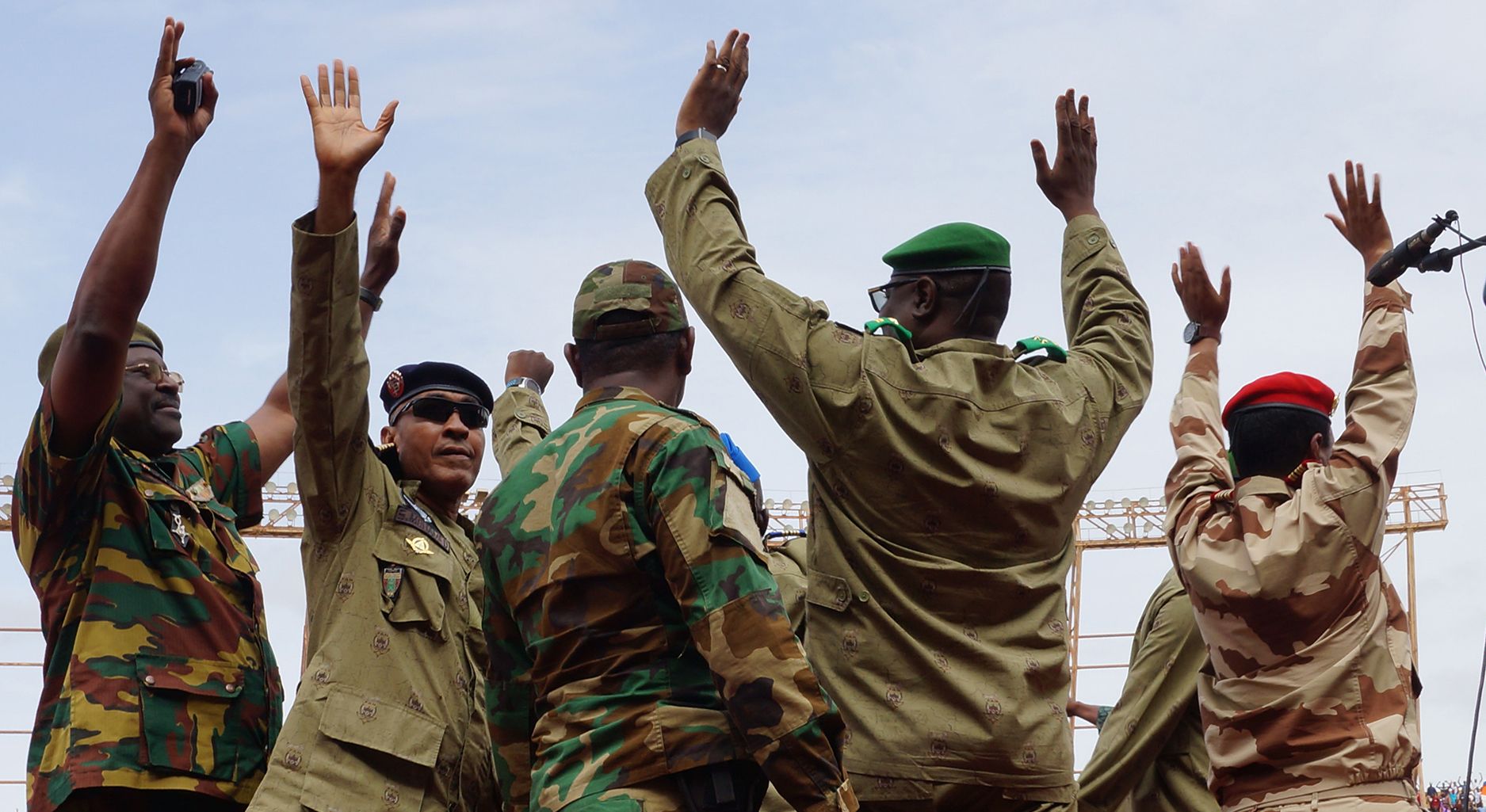 Men in military uniforms on stage, raising their hands in the air.