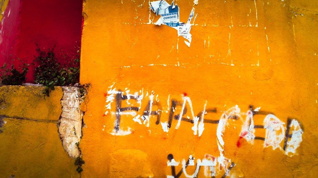 Orange-rote Wand mit schwarzer Schrift FARC-EP, darüber weiße Farbe und Spuren von roter Farbe.