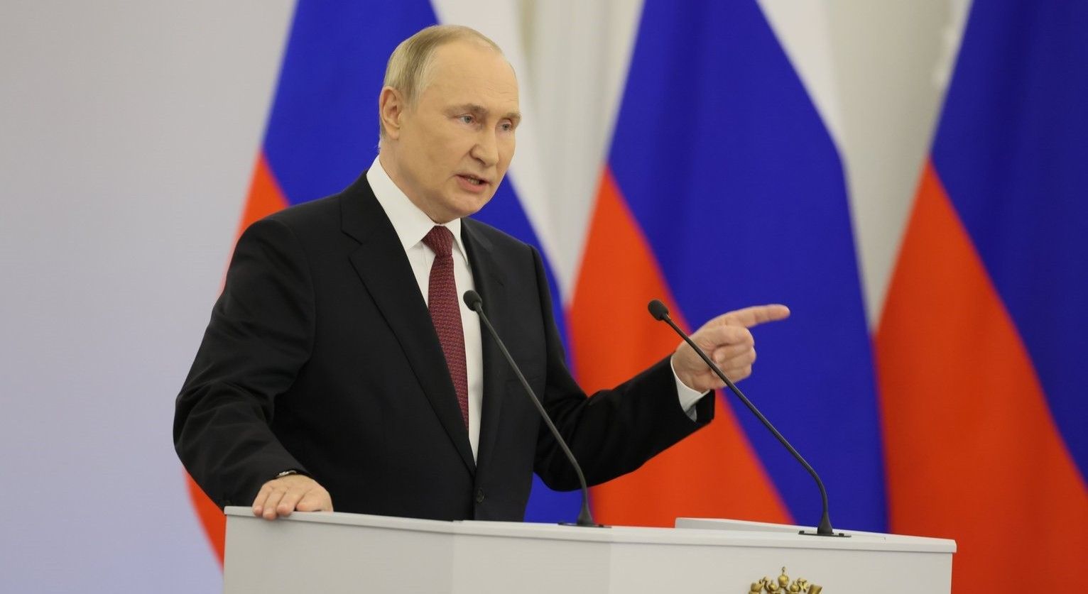 Putin steht an einem Rednerpult und spricht. Im Hintergrund sind russische Flaggen zu erkennen.