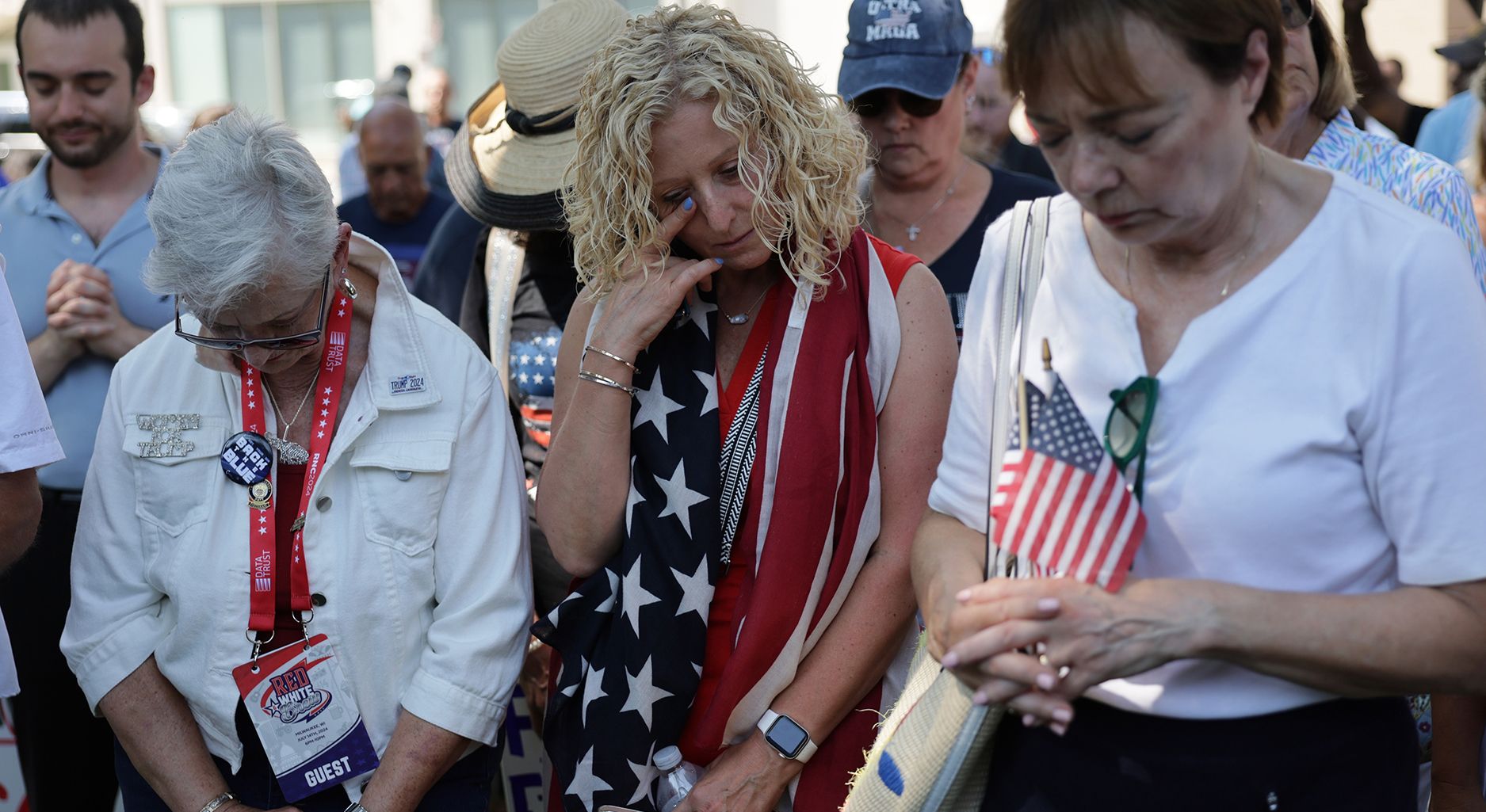 Menschen mit amerikanischer Flagge neigen den Kopf und haben die Hände verschränkt wie zum Gebet.