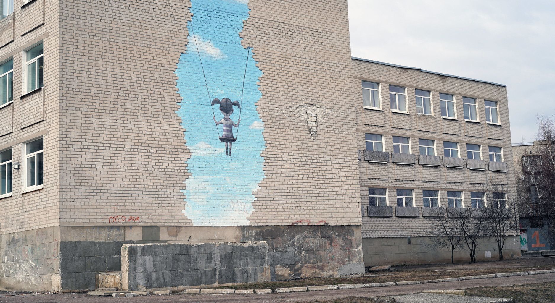 Wand eines grauen Gebäudes mit Gemälde eines blauen Himmels, vor dem ein Kind schaukelt