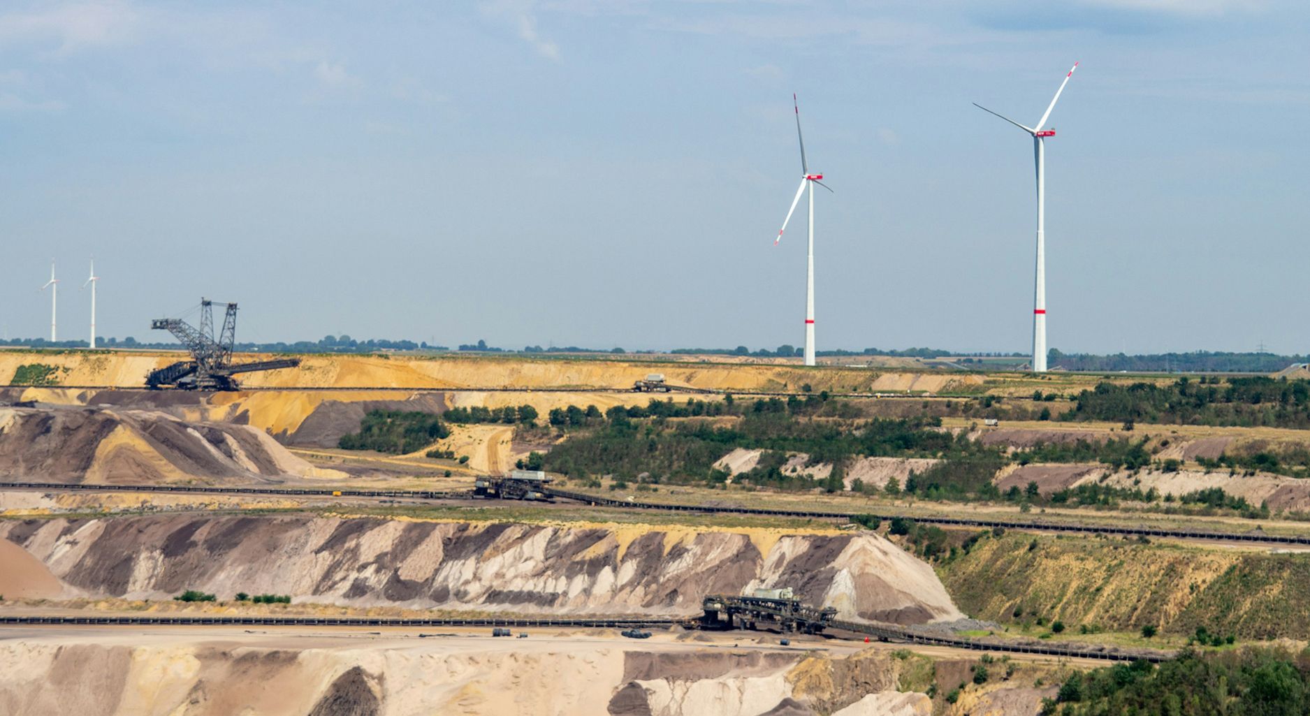 Ein Braunkohletagebau im Vordergrund, im Hintergrund Windkraftanlagen.