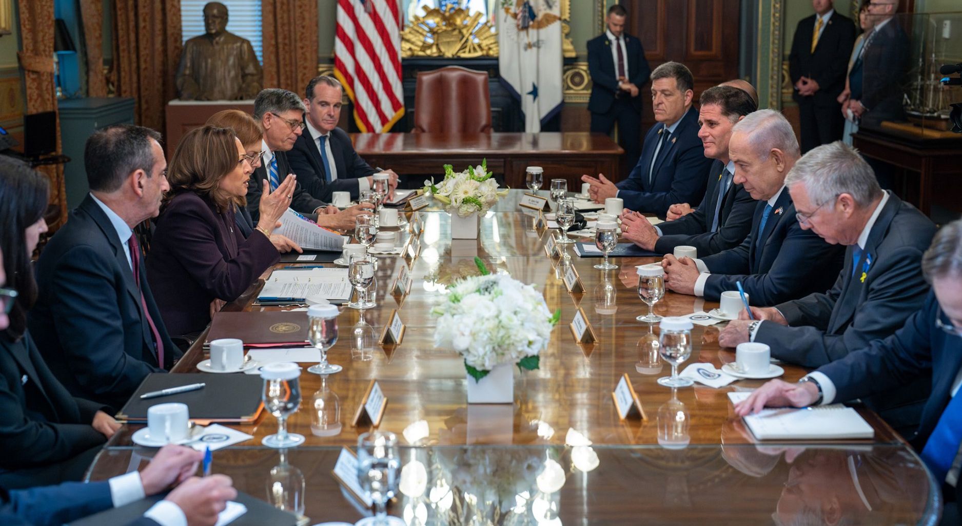 Eine Gruppe Menschen sitzt um einen großen Konferenztisch herum. Auf der linken Seite sitzt eine US-Delegation um Kamala Harris,auf der rechten Seite sitzt eine israelische Delegation um Benjamin Netanjahu