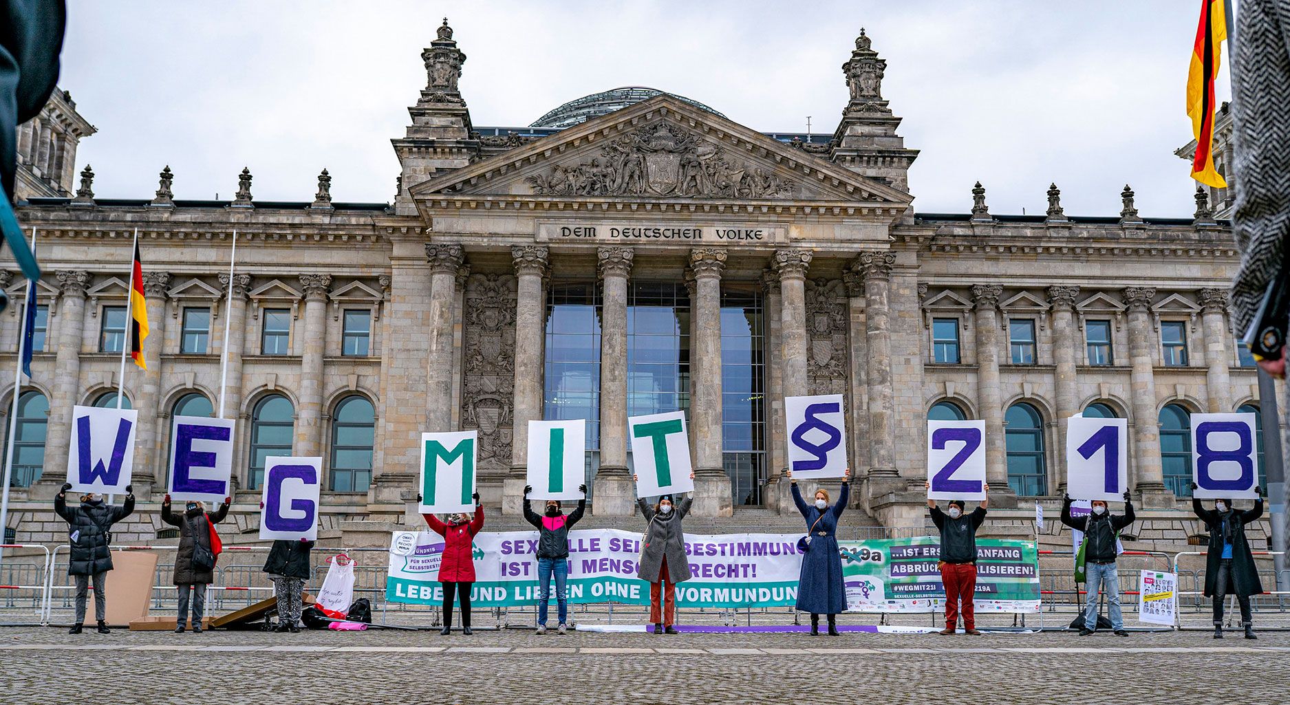Protestierende vor dem Reichstagsgebäude in Berlin halten Schilder hoch, aus denen sich zusammengesetzt der Text ergibt "Weg mit §218"