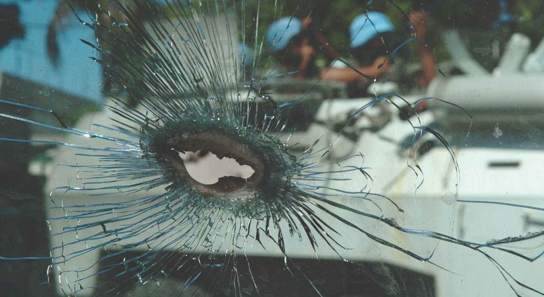 Im Vordergrund Loch und Splitter in einer Glasscheibe, im Hintergrund ein Tankwagen der UN mit UN-Soldaten, der im Viertel Bel-Air von Anhängern Aristides angegriffen wird.