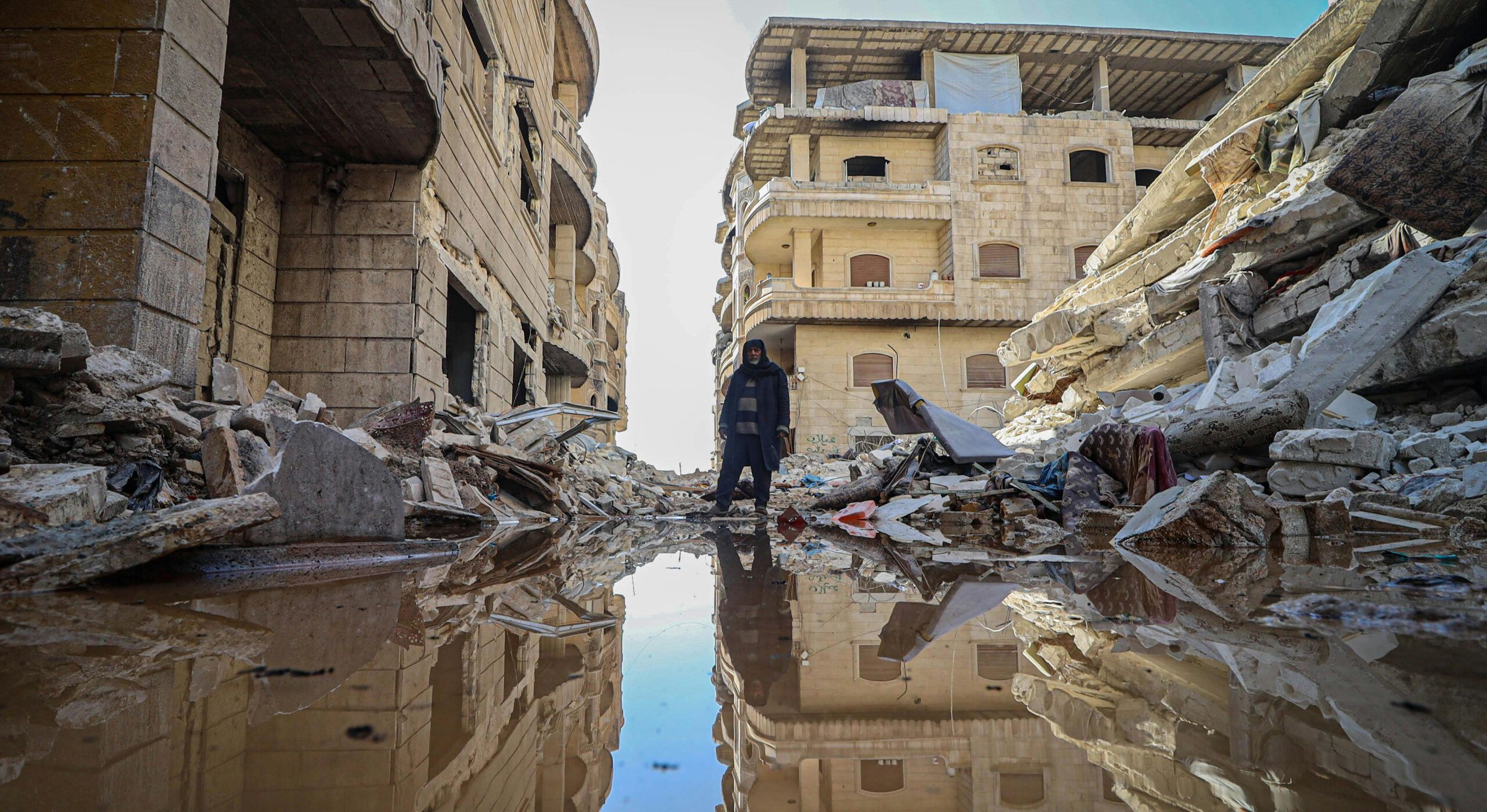 A man standing on a street in between ruins and destroyed buildings. The stree