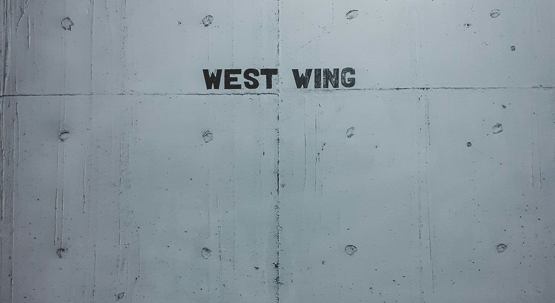 Graue Wand auf der in schwarzen Großbuchstaben „WEST WING“ steht.