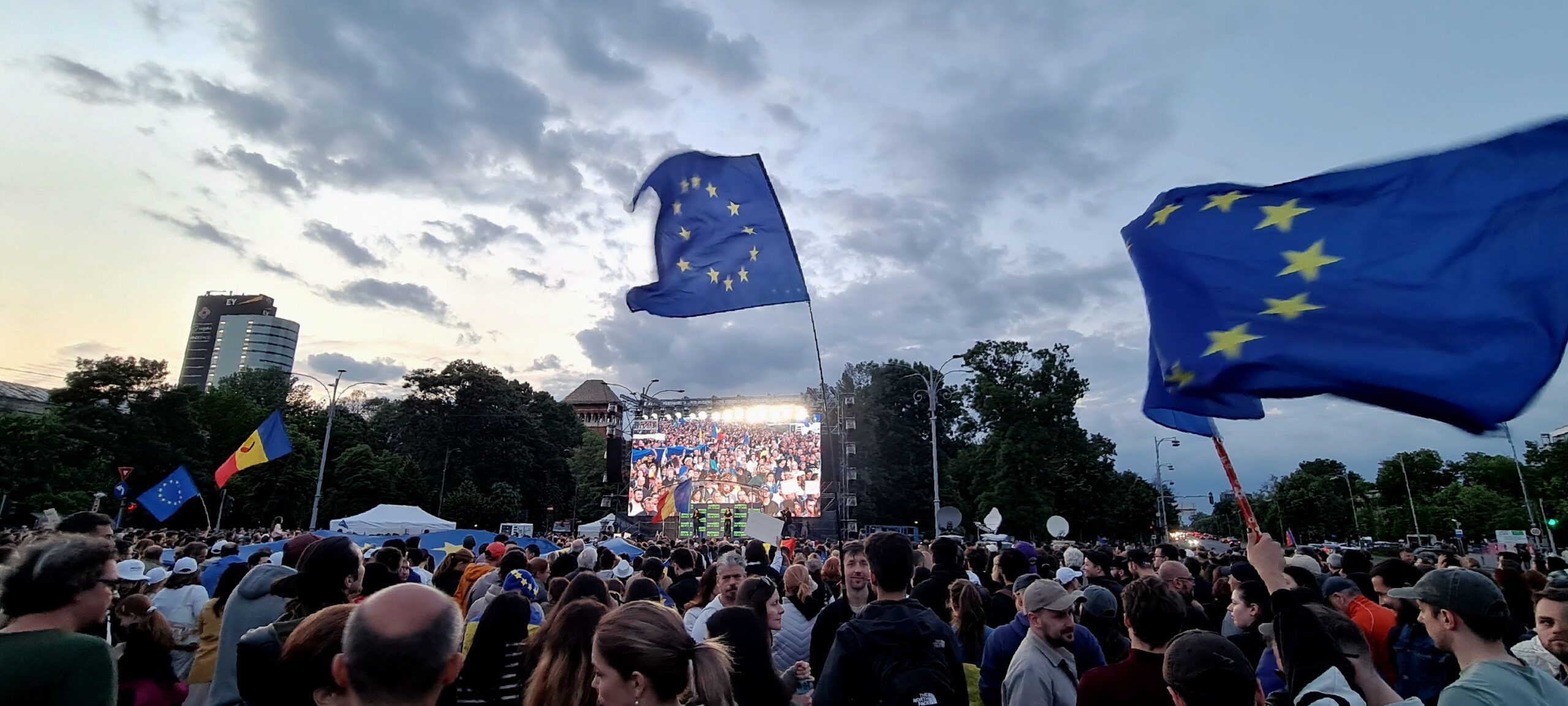 Crowd of people in front of a big screen with European flags.
