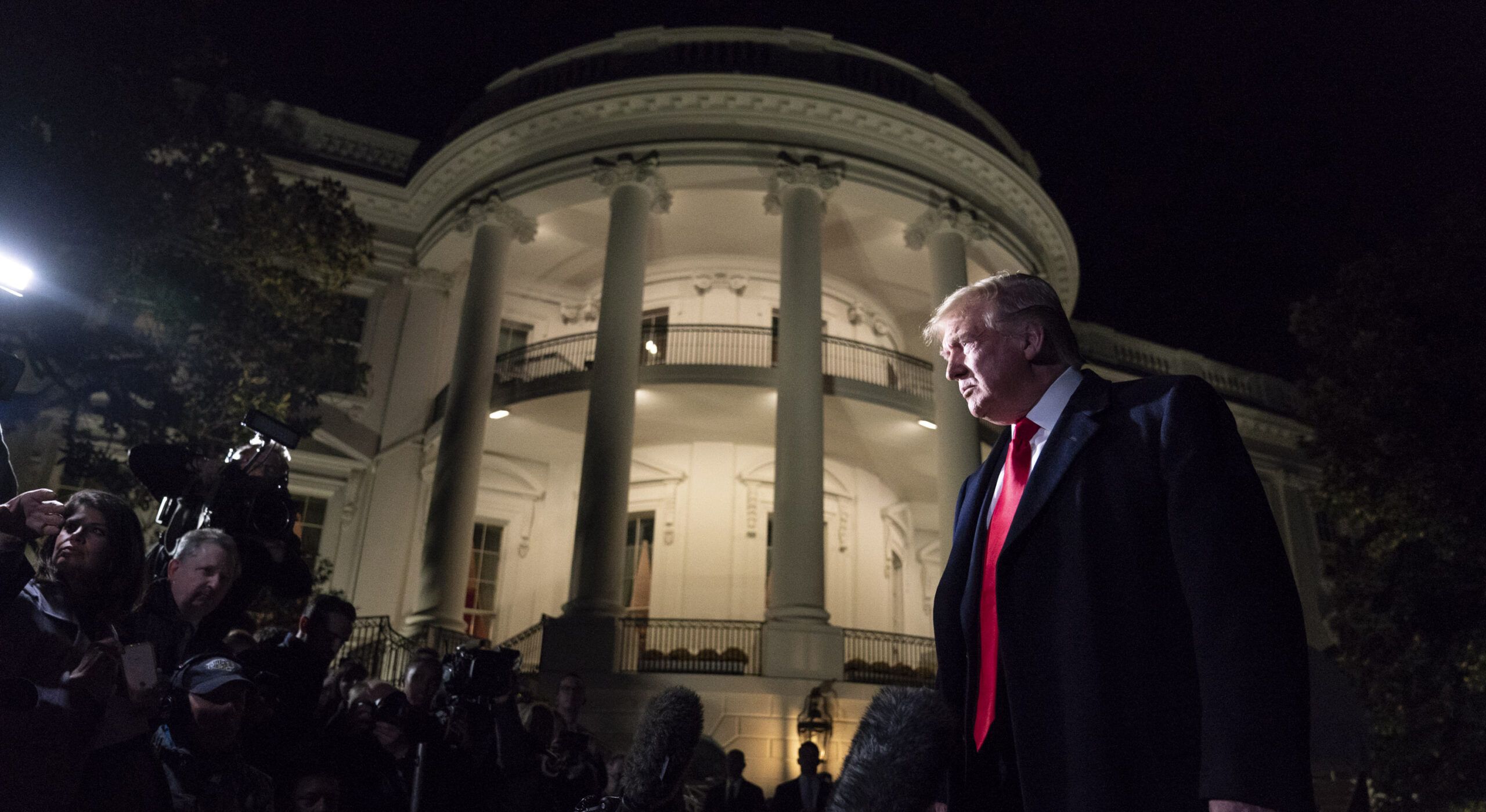 Night-time shot of President Trump in front of the White House and next to some reporte´rs