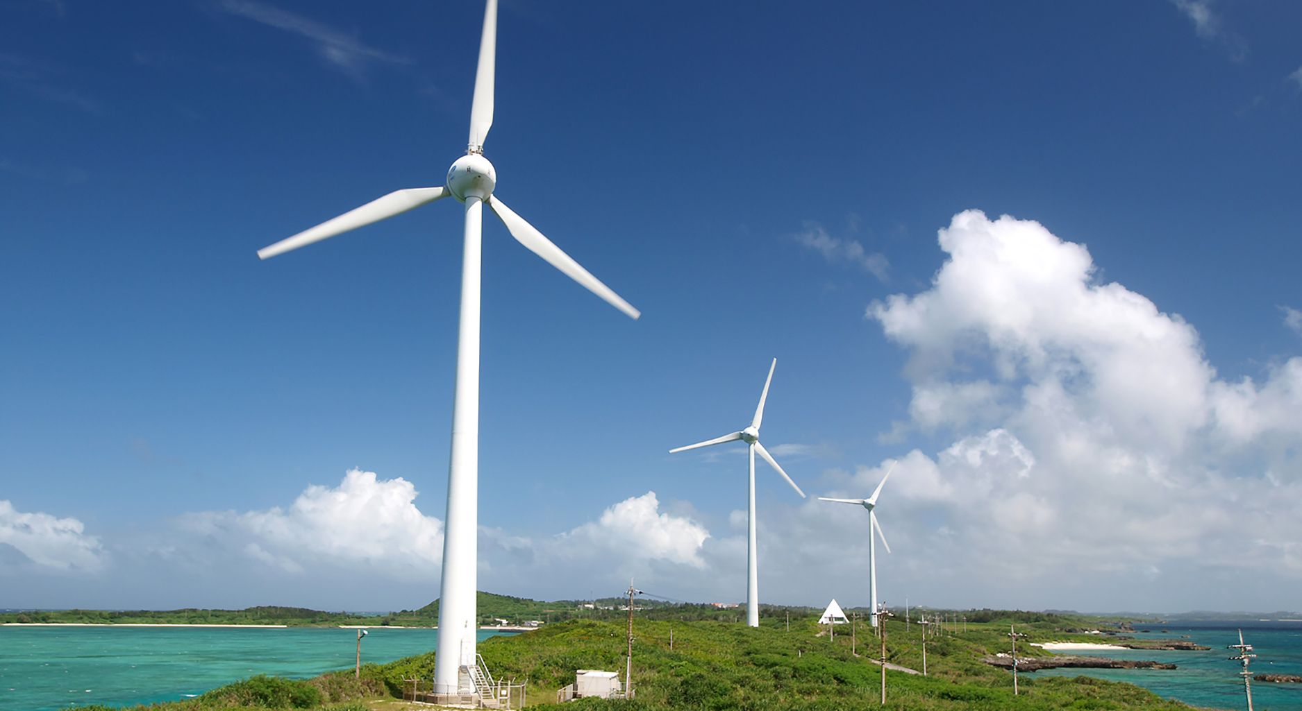 Wind turbines stand on a sandy strip of land in a turquoise water with a clear blue sky. A banner reads socio-ecological transformation.
