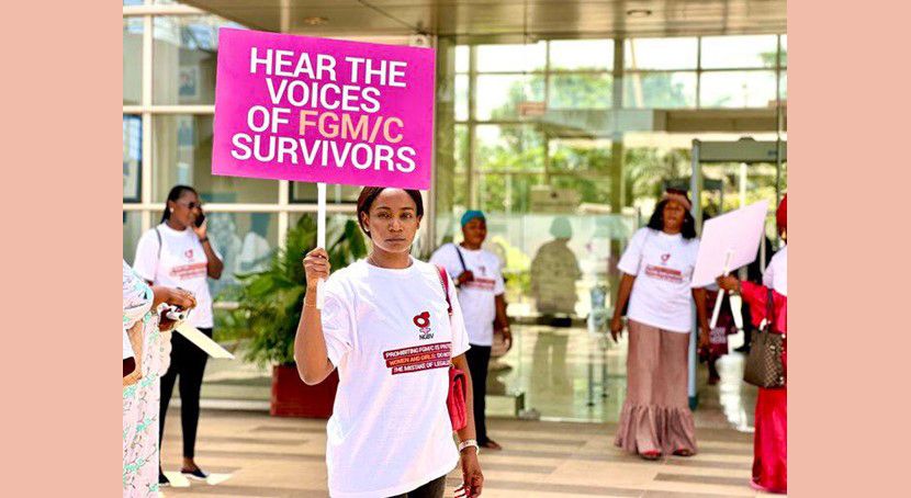 Photo of women with matching t-shirts, one is holding up a sign that says "Hear the voices of FGM/C survivors"