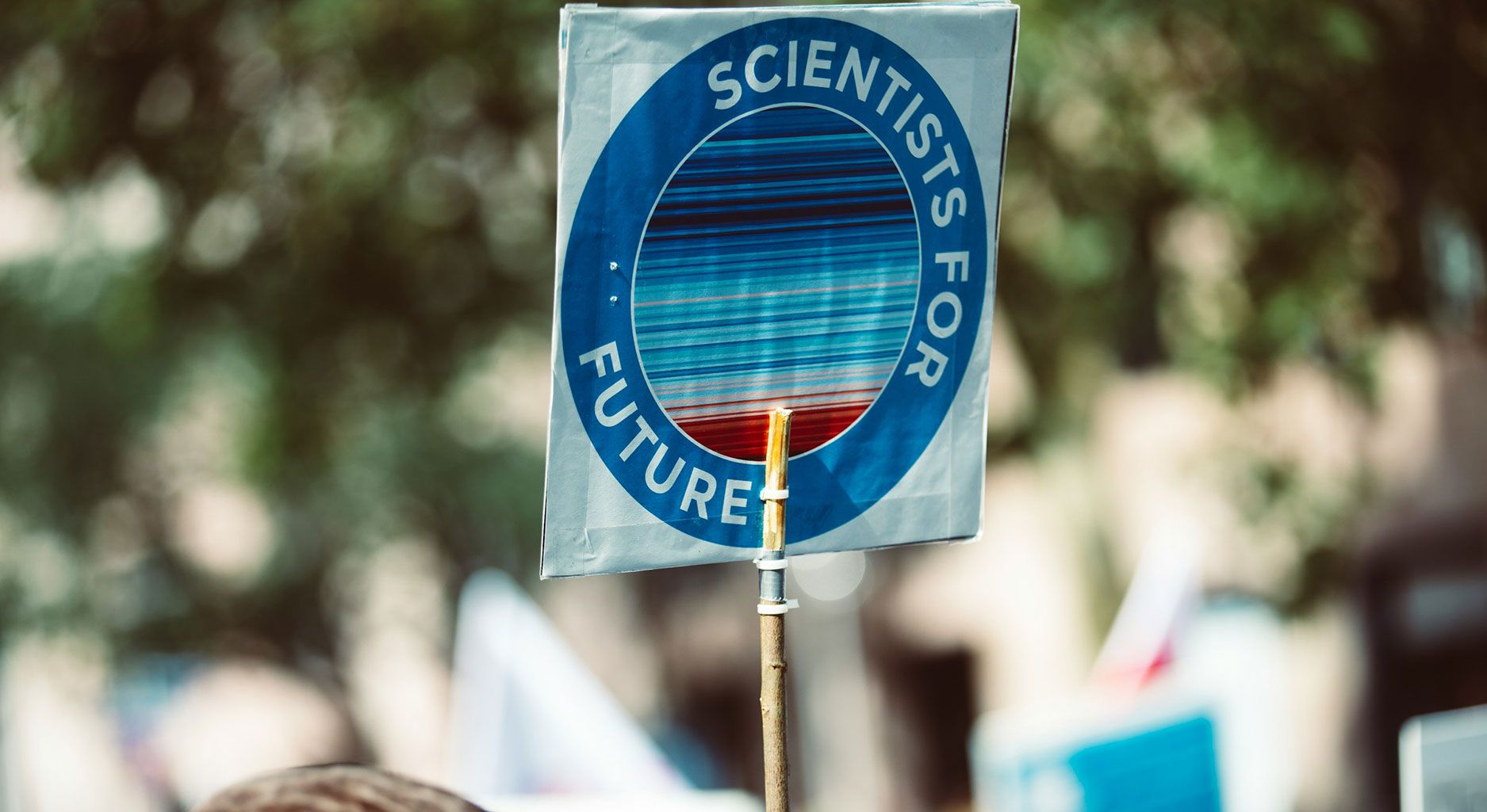 Ein Schild mit der Aufschrift Scientists for Future in einem Kreis um eine Grafik aus verschiedenen Blautönen und unten Rottönen herum, die den durchschnittlichen Temperaturanstieg darstellen