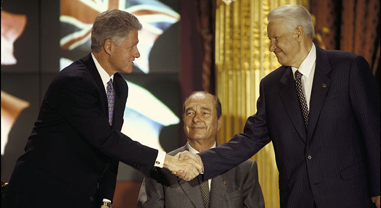 Das Bild zeigt den US-Präsidenten Clinton, französischen Präsidenten Chirac und russischen Präsidenten Jelzin beim NATO-Russland-Gipfel 1997. Clinton und Chirac schütteln Hände.