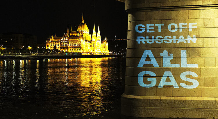 Foto zeigt die Donau und im Hintergrund das Parlamentsgebäude in Budapest, im Vordergrund einen Brückenpfeiler mit der darauf gesprühten Aufschrift "Get off Russian (durchgestrichen) All Gas"