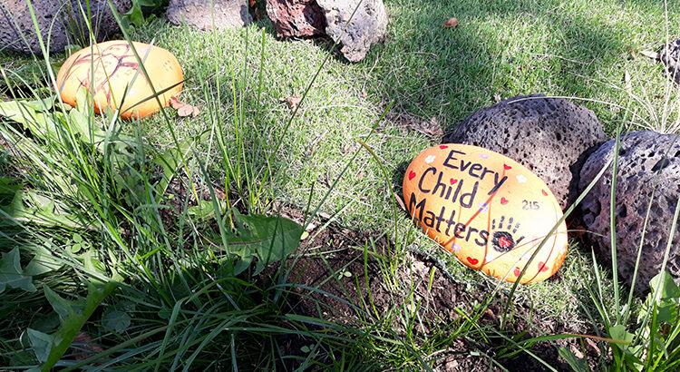 Meadow with painted stones on which is written "Every child matters".