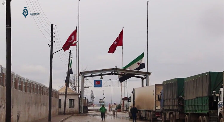 Grenzübergang mit syrischen und türkischen Flaggen und Fahrzeugen.