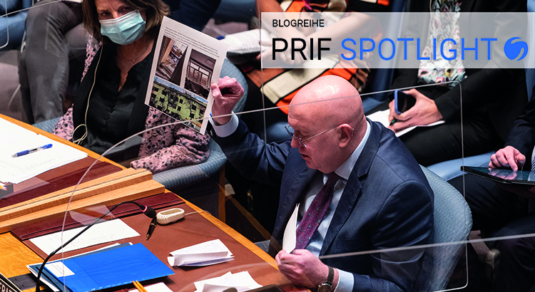 Russian Ambassador sits at the Security Council, holding a printed page with images up in the air.