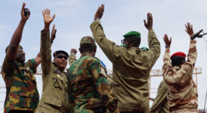 Men in military uniforms on stage, raising their hands in the air.