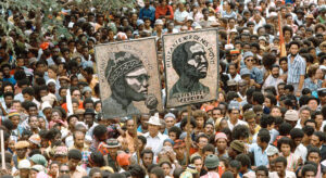 a large crowd holding up two posters showing the head of two men.
