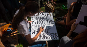 A young woman draws a poster saying "Climate Change is not the Change we are looking for"