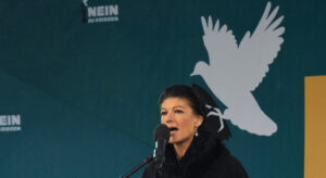 Sahra Wagenknecht mit Mikrofon auf einer Kundgebung. Im Hintergrund zu sehen eine Friedenstaube und der Slogen "Nein zu Kriegen".