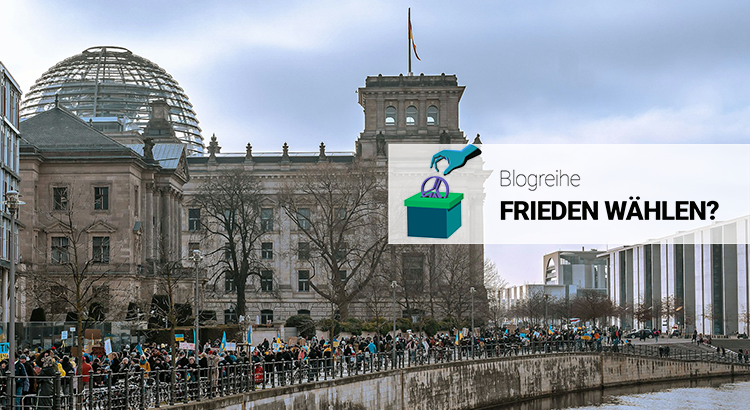 Eine große Gruppe Menschen mit Plakaten, die die Ukraine-Flagge zeigen, laufen links nebem einem Fluss entlang. Im Hintergrund ist das Gebäude des Deutschen Bundestags mit der Glaskuppen zu sehen.