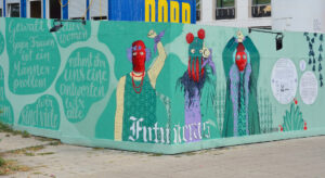 Grafitti von drei vermummten Frauen an einem Bauzaun mit erhobenen Fäusten. Der Schriftzug liest: Zukunft auf spanisch.