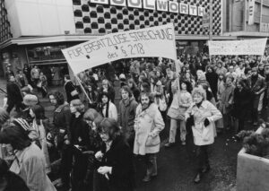 Schwarzweißfoto von demonstrierenden Menschen. Im Vordergrund ist ein Banner sichtbar, auf dem steht "Für ersatzlose Streichung des §218"