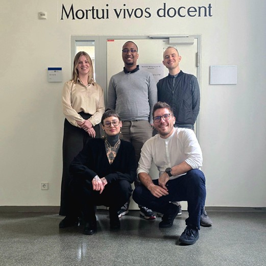 A group of five people standing in front of a wall with the writing "Mortui vivos docent"