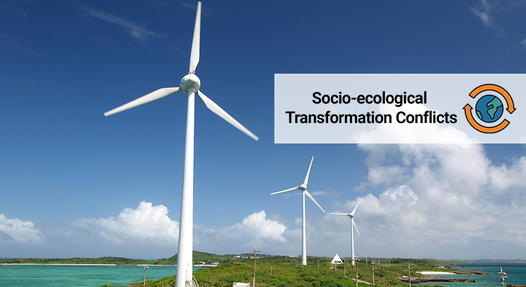 Wind turbines stand on a sandy strip of land in a turquoise water with a clear blue sky. A banner reads socio-ecological transformation.