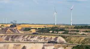 Ein Braunkohletagebau im Vordergrund, im Hintergrund Windkraftanlagen.