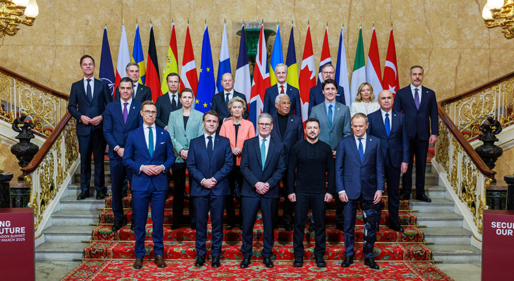 Gruppenfoto formell gekleideter Personen auf einer Treppe vor einer Reihe von Flaggen.