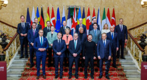 Gruppenfoto formell gekleideter Personen auf einer Treppe vor einer Reihe von Flaggen.