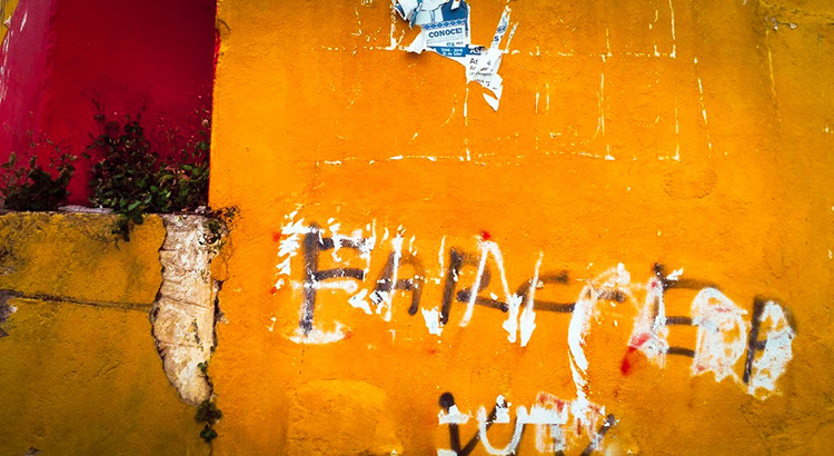 Orange-rote Wand mit schwarzer Schrift FARC-EP, darüber weiße Farbe und Spuren von roter Farbe.