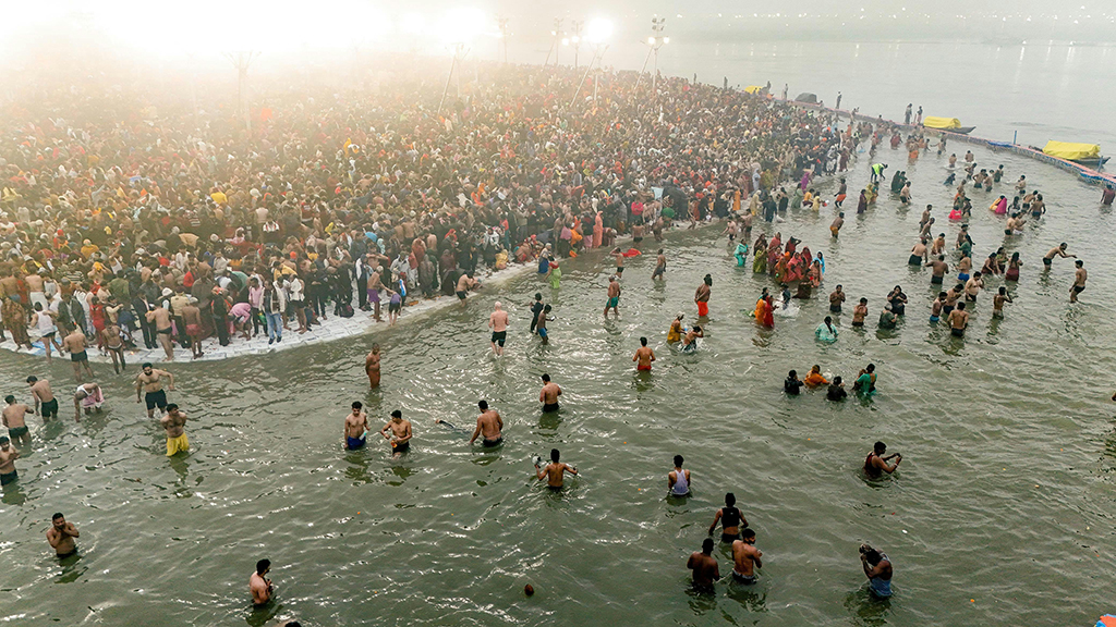 Photo of a large crowd of people at the shore of a river, some of which are bathing.