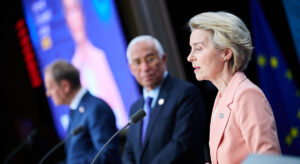Photo that shows Donald Tusk, Polish Prime Minister, Antonio Costa, President of the European Council, and Ursula von der Leyen on a stage speaking into a microphone.