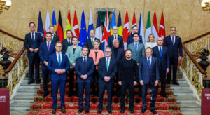 Group photo of formally dressed people on a staircase in front of a row of flags.