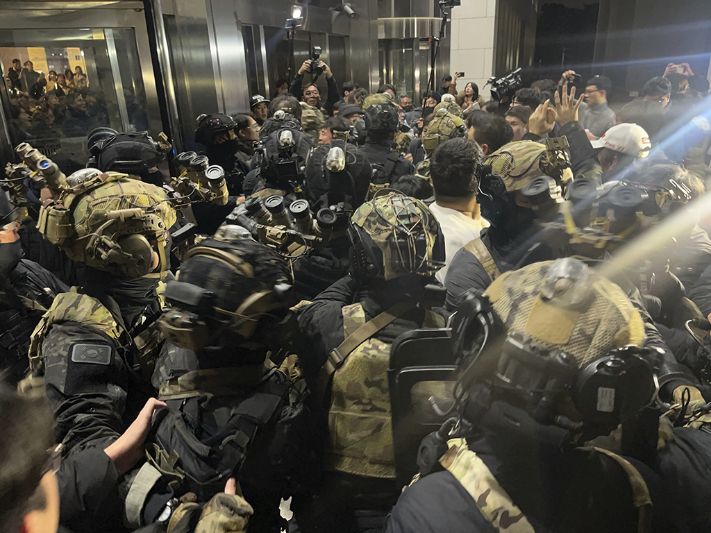 Foto einer Menschenmenge, einige Personen im Vordergrund tragen militärische Ausrüstung, dahinter stehen einige Personen mit Fotokameras.