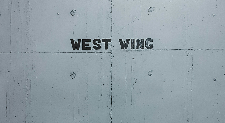Graue Wand auf der in schwarzen Großbuchstaben „WEST WING“ steht.