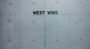 Graue Wand auf der in schwarzen Großbuchstaben „WEST WING“ steht.