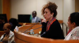 Thania Paffenholz sitting in a large conference room and talking through a microfone